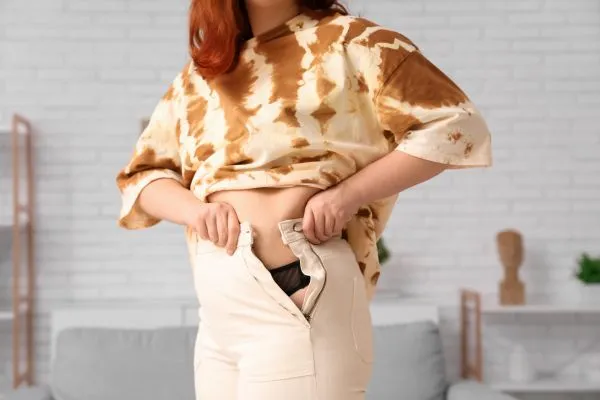 Image of woman trying to do her trousers up after pregnancy weight gain Grays