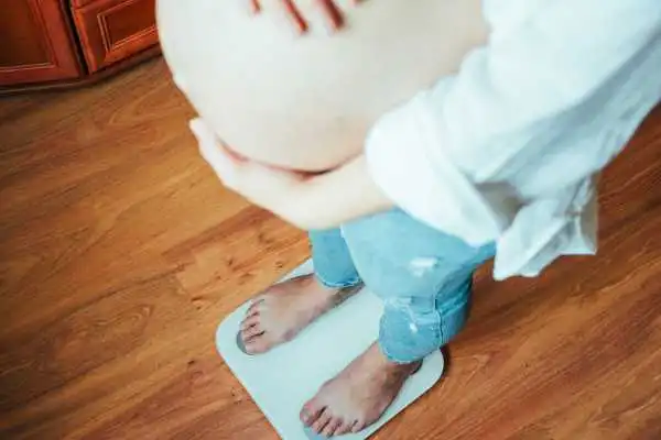 Image of woman weighing herself and experiencing weight gain through pregnancy Grays